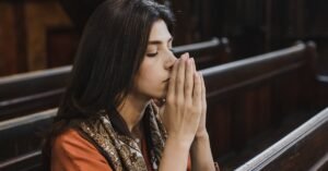 Brunette woman in quiet prayer at a cathedral, seated in a wooden pew.